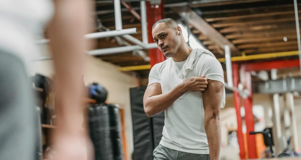 Ein Mann betrachtet im Spiegel eine muskuläre Schwachstelle, die er durch gezieltes Training beseitigen möchte.