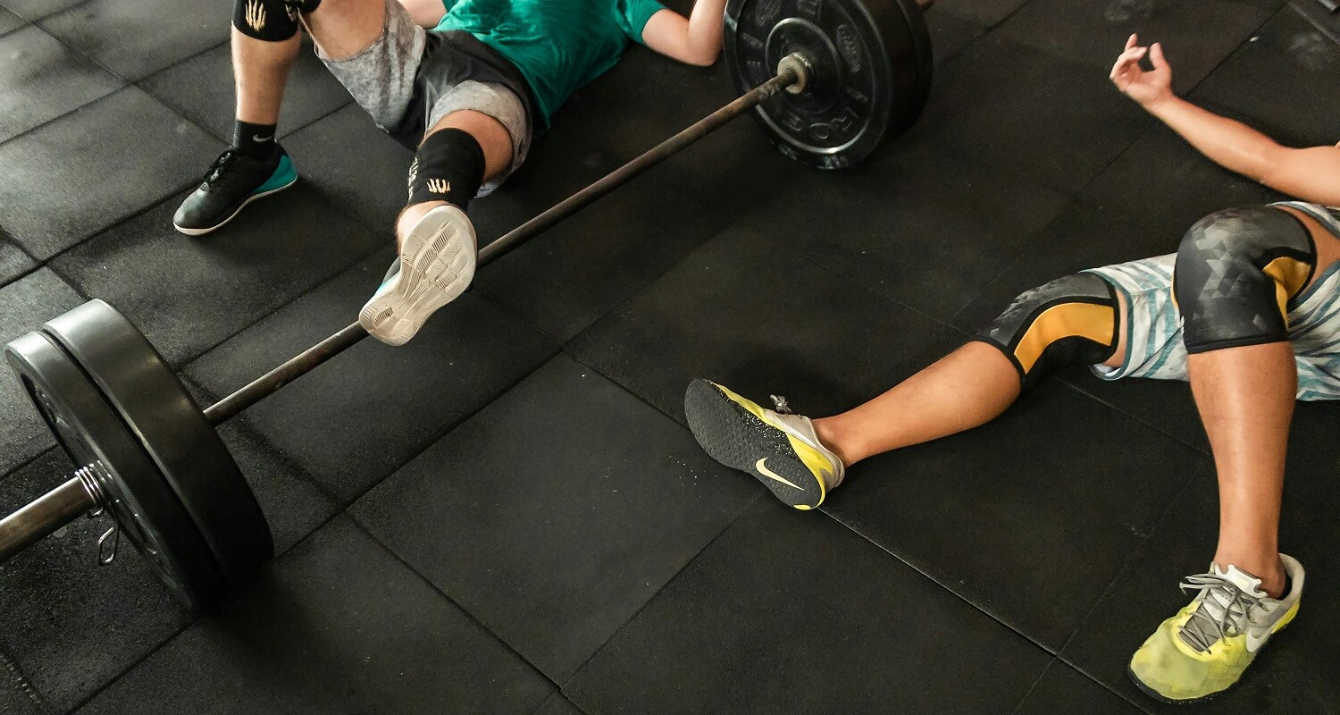 Zwei Sportler liegen erschöpft am Boden, nachdem sie zuerst ein Krafttraining und dann direkt danach noch ein CrossFit-Training absolviert haben statt ihr Hybrid-Training aufzuteilen.